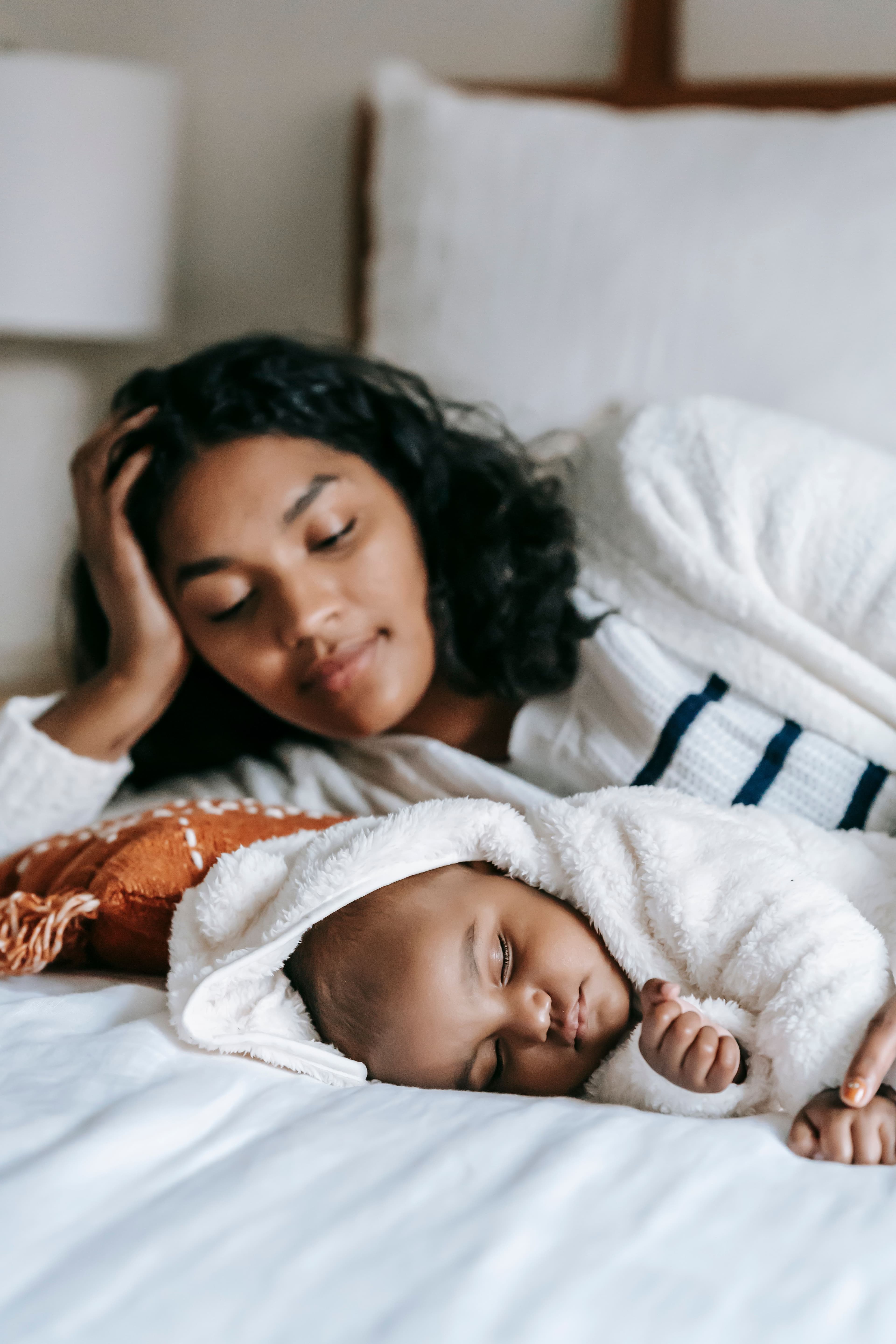 A mother lying on the bed watching her sleeping newborn