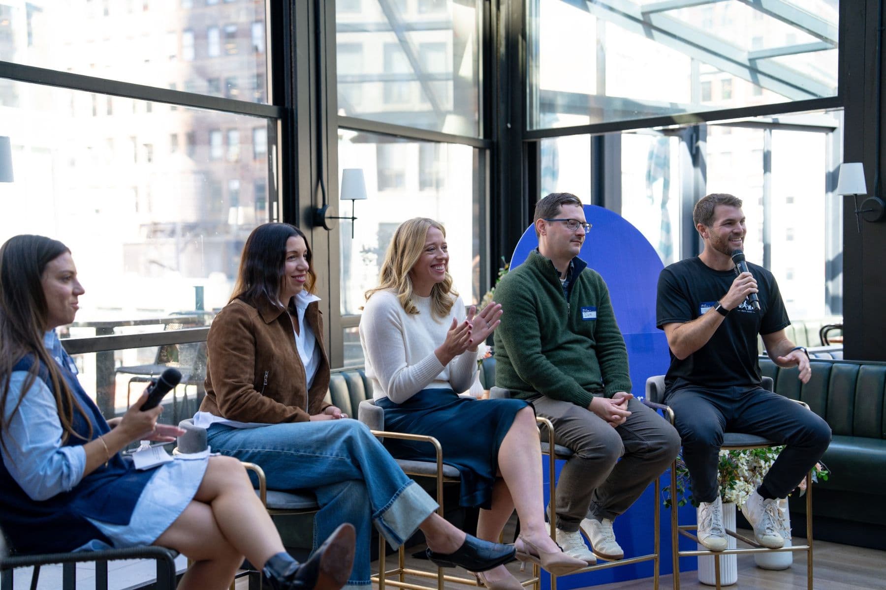 Five panelists seated in a row, one holding a microphone and smiling