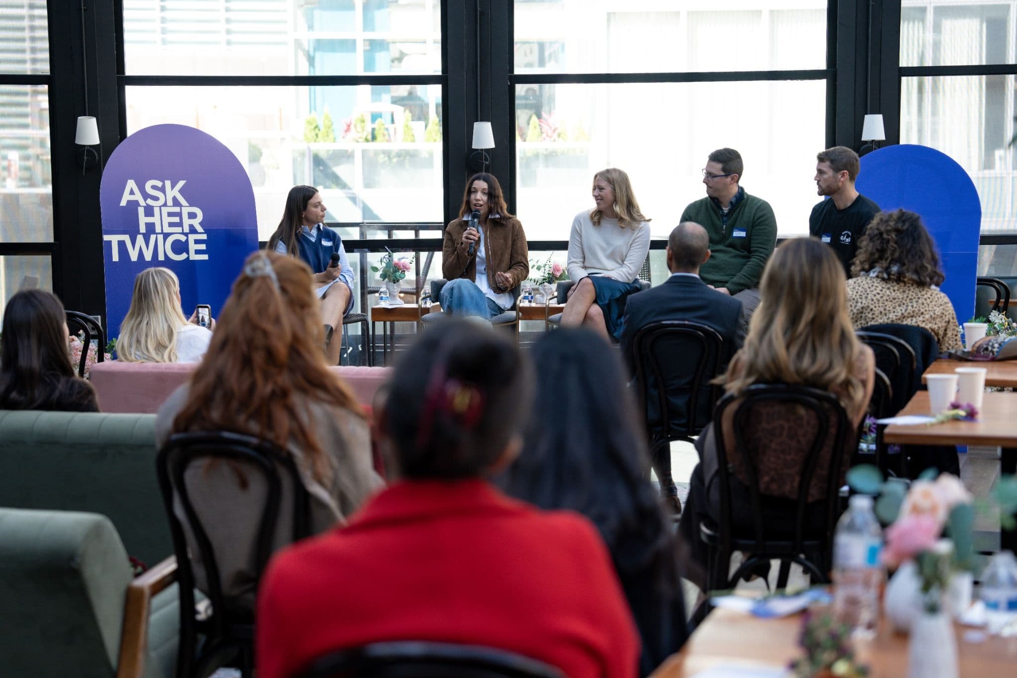 Guests watch a panel in front of a large Ask Her Twice banner