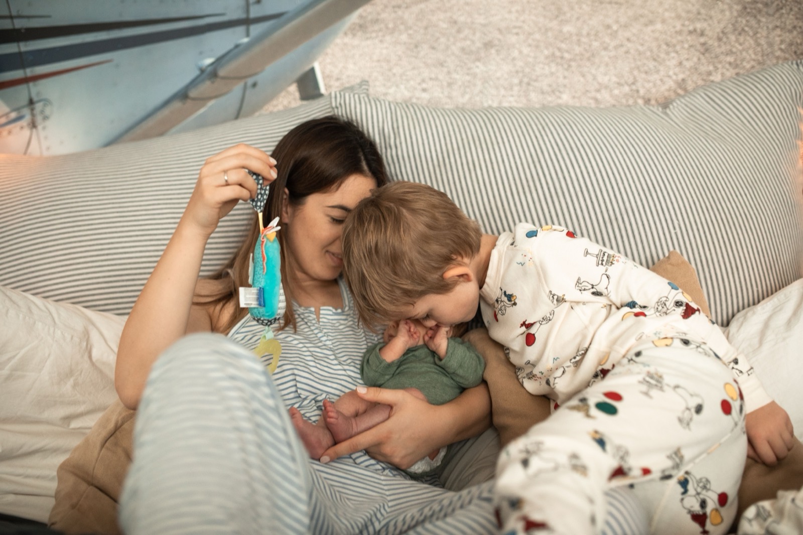 A mother lying in bed playing with her toddler and newborn