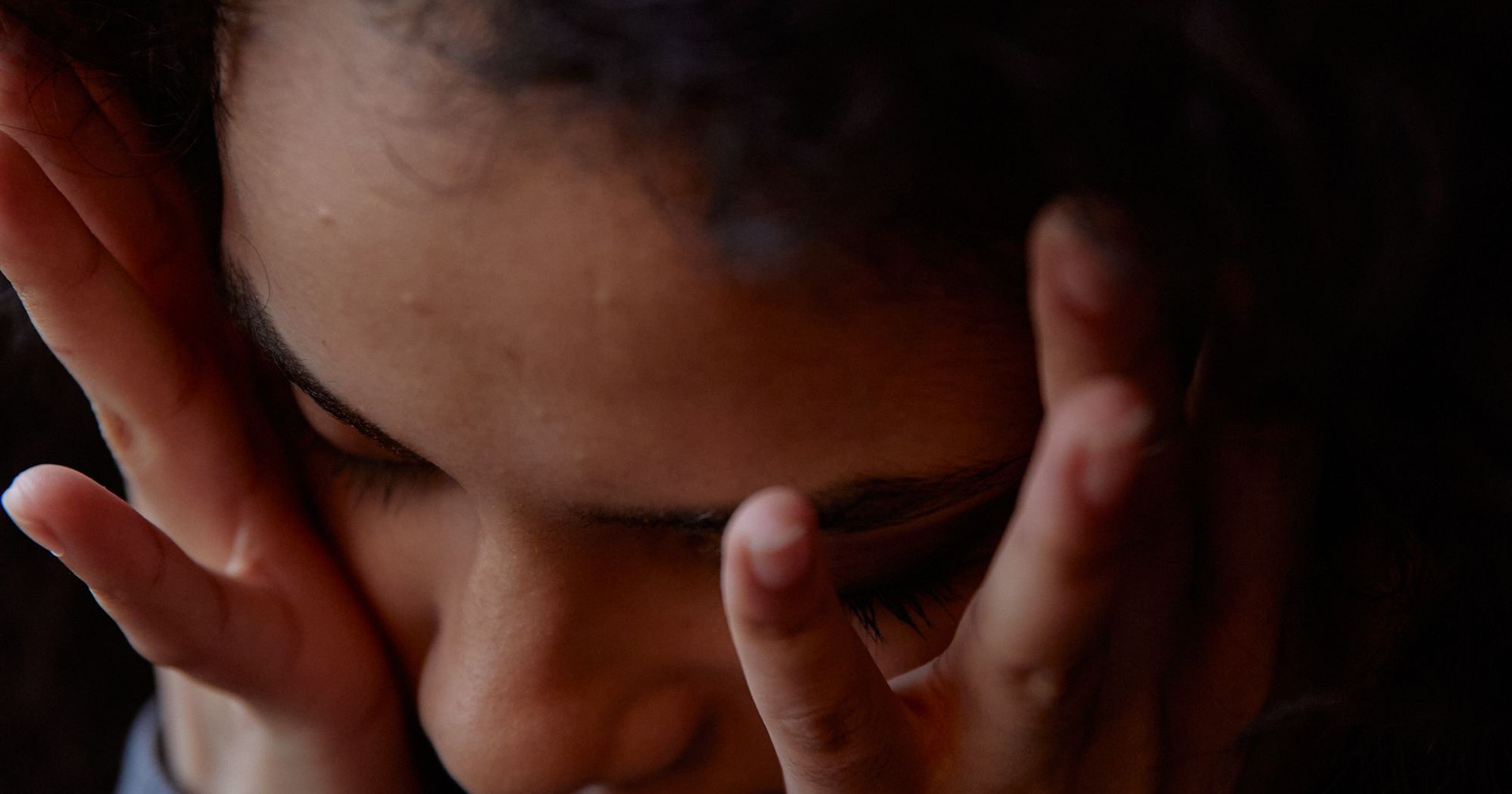 A woman with her head resting in her hands, eyes closed, in dim light