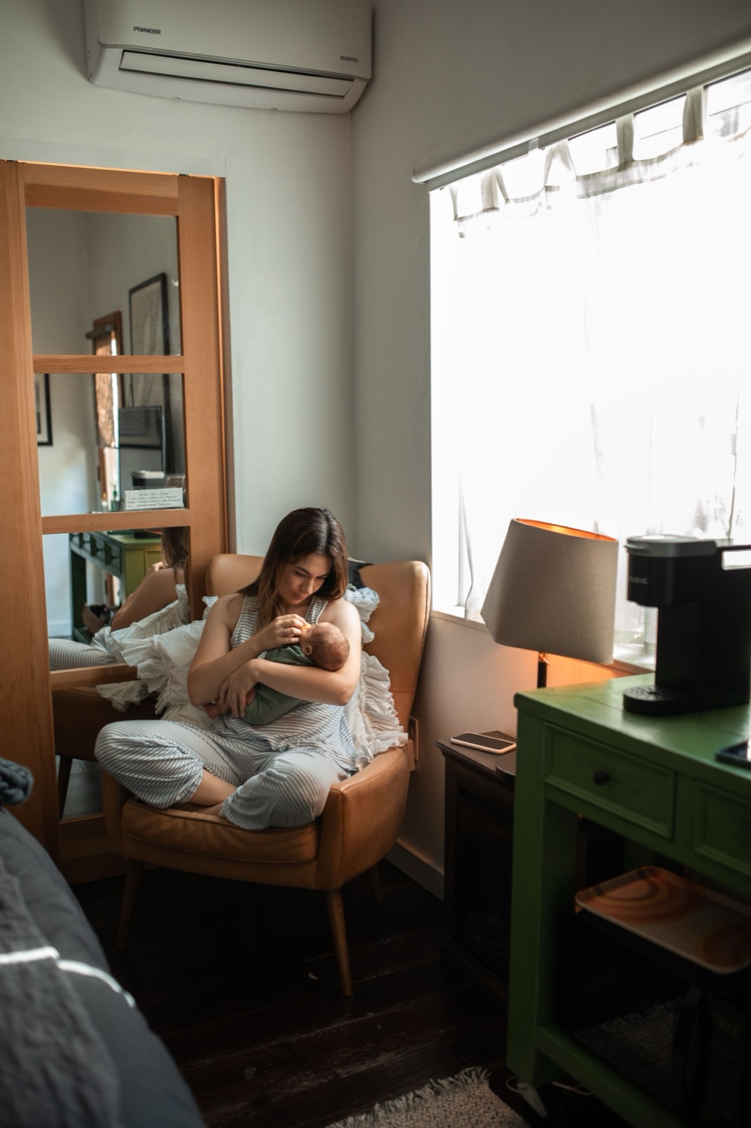 A mother sitting in a chair holding her newborn in a quiet room by the window