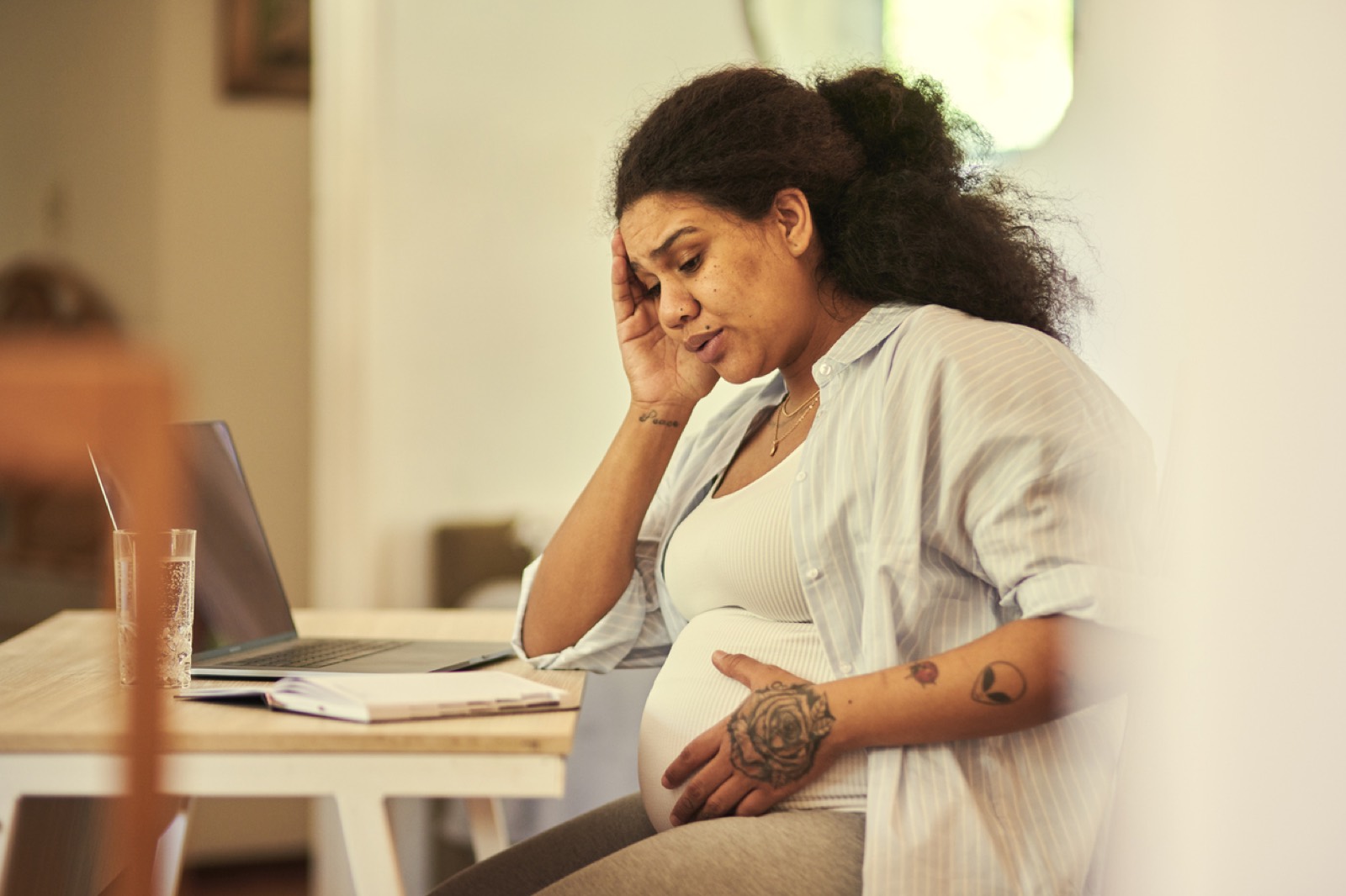 A pregnant woman resting her head in her hand at a laptop, looking overwhelmed