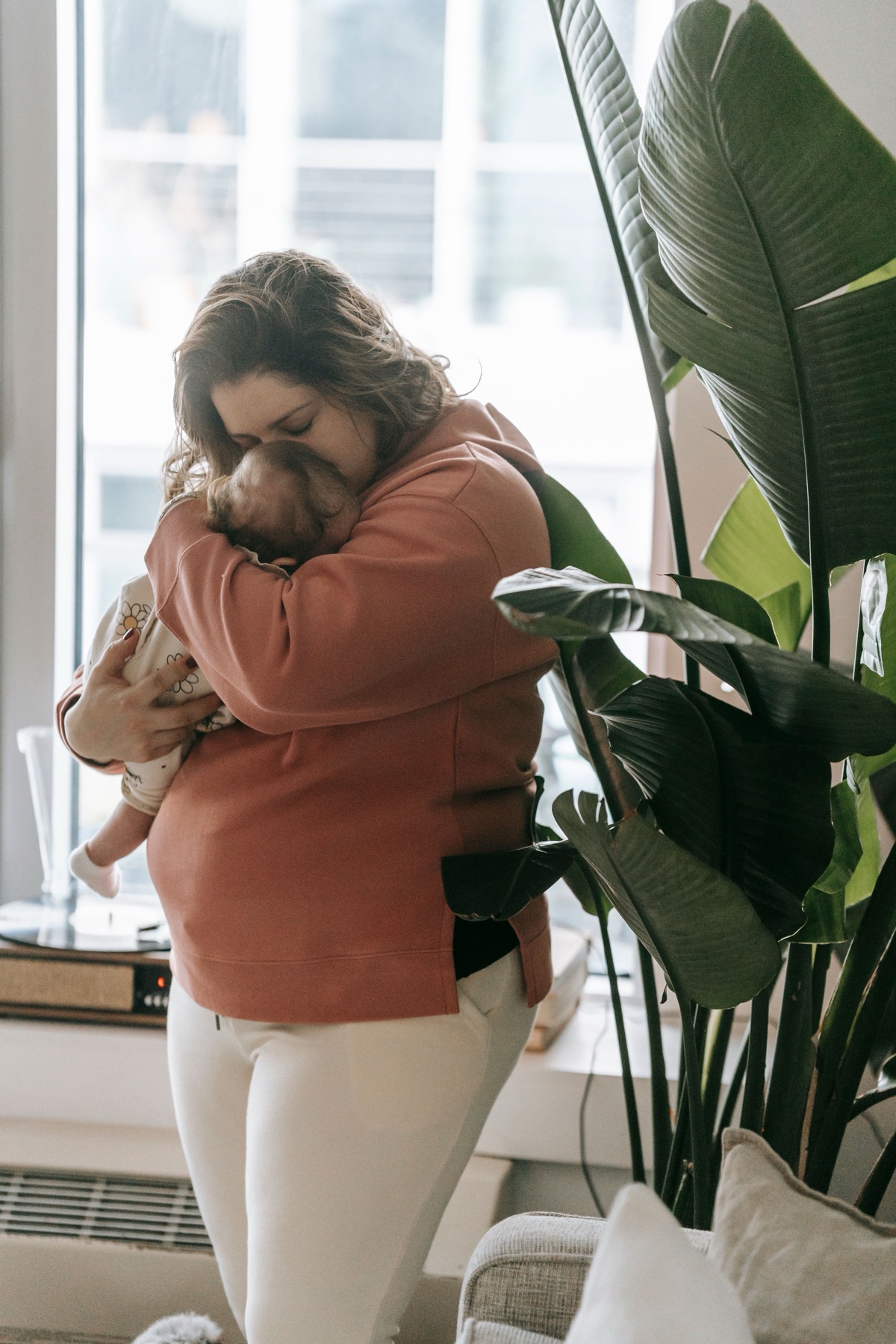 A mother holding her newborn close, by a sunlit window.
